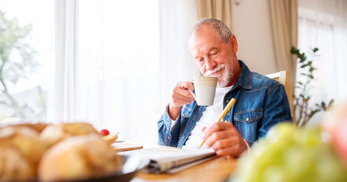 Senior man enjoying a cup of coffee while reading a newspaper at the breakfast table.